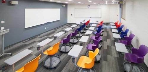 an empty classroom with purple and orange desk chairs facing a whiteboard